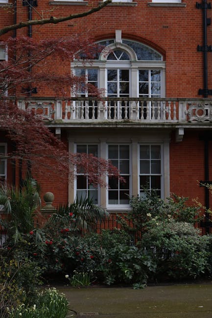 A detailed view of a historic glass and metal conservatory roof with intricate decorative trim and a prominent spire at the top, showcasing curved, segmented panes of glass supported by white-painted